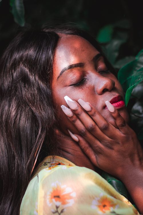 Free Side view of calm African American woman with long shiny air touching cheek and closing eyes in soft light Stock Photo