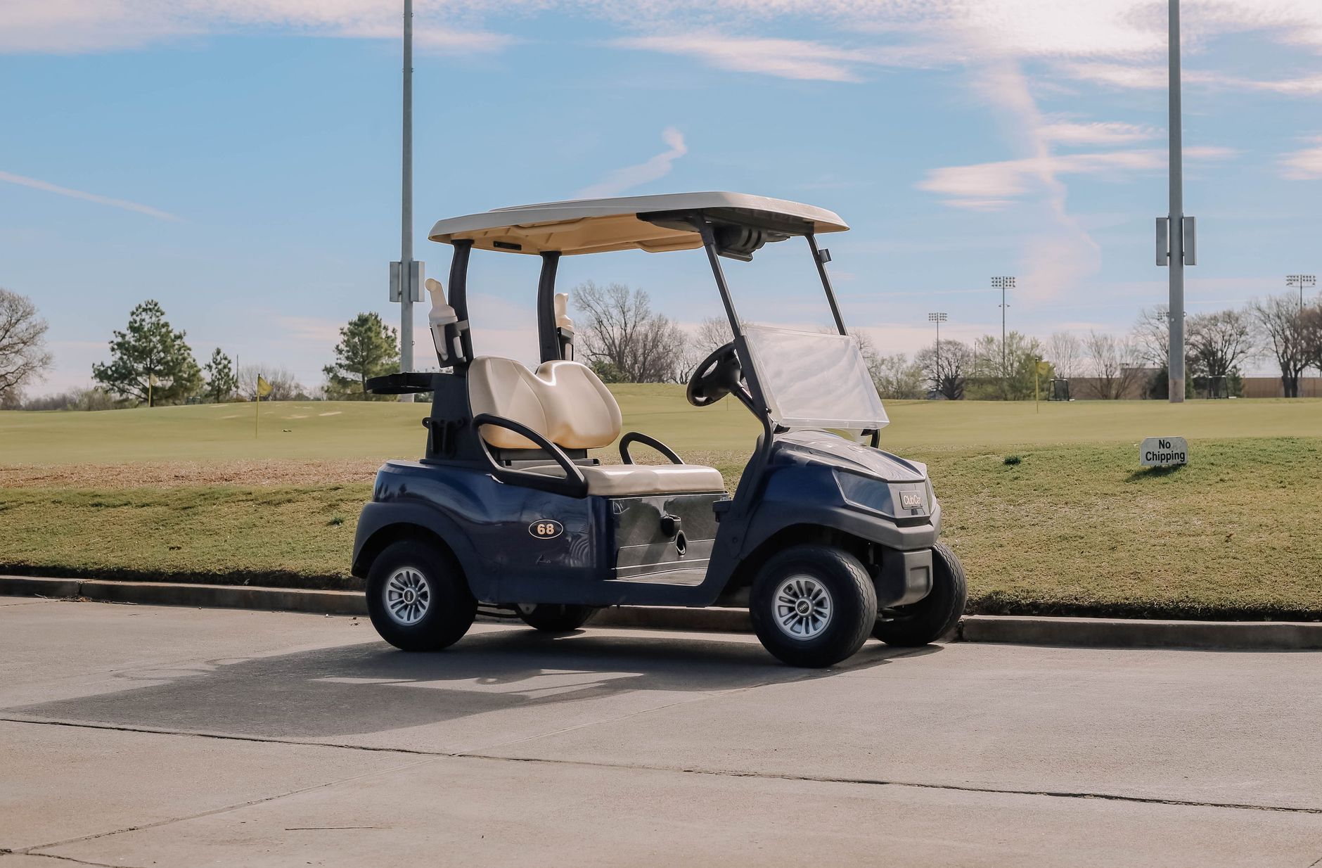 A golf cart parked on a pathway next to a golf course under a clear blue sky.