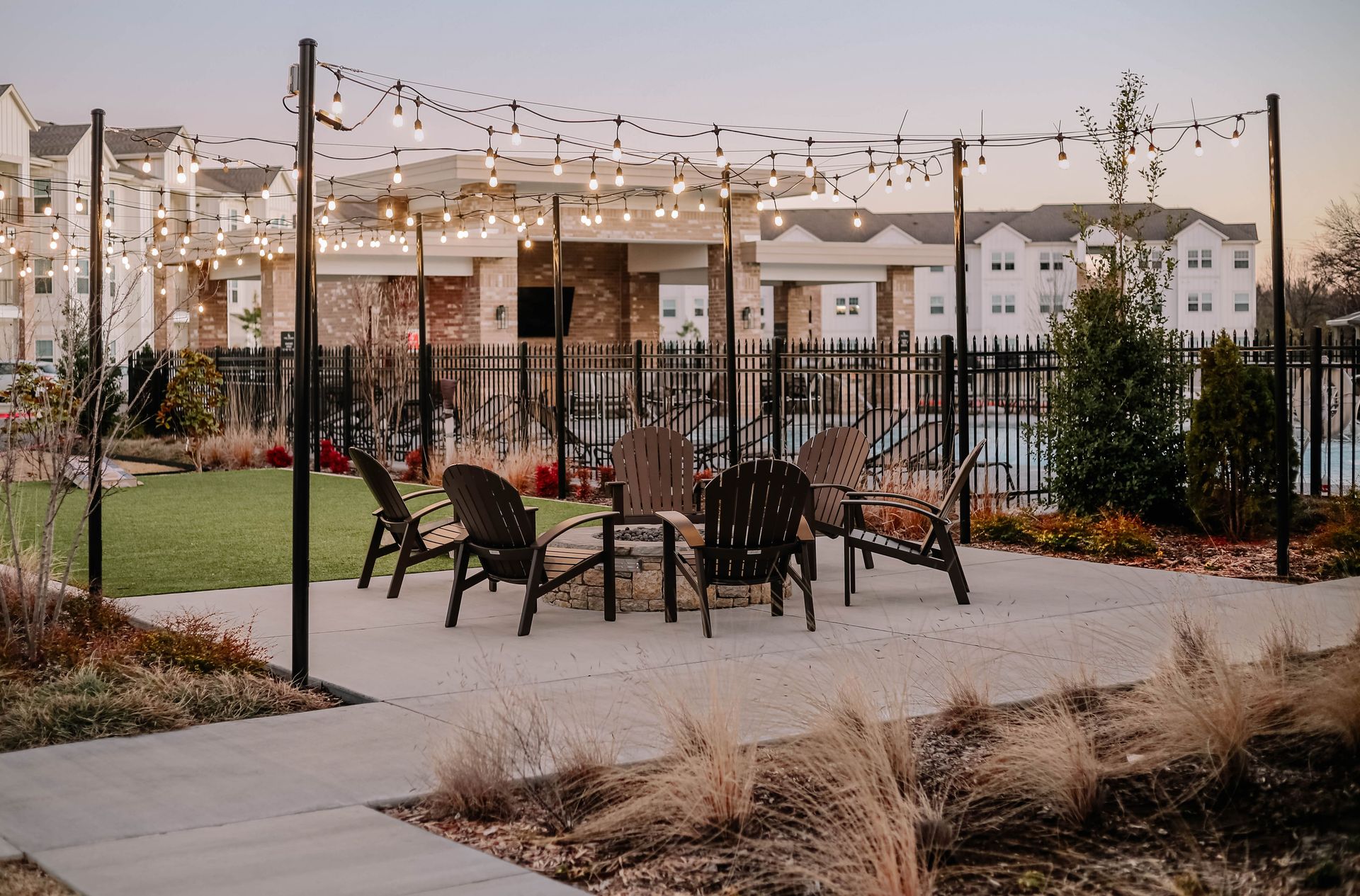 Outdoor lounge chairs and a fire pit beneath string lights at dusk