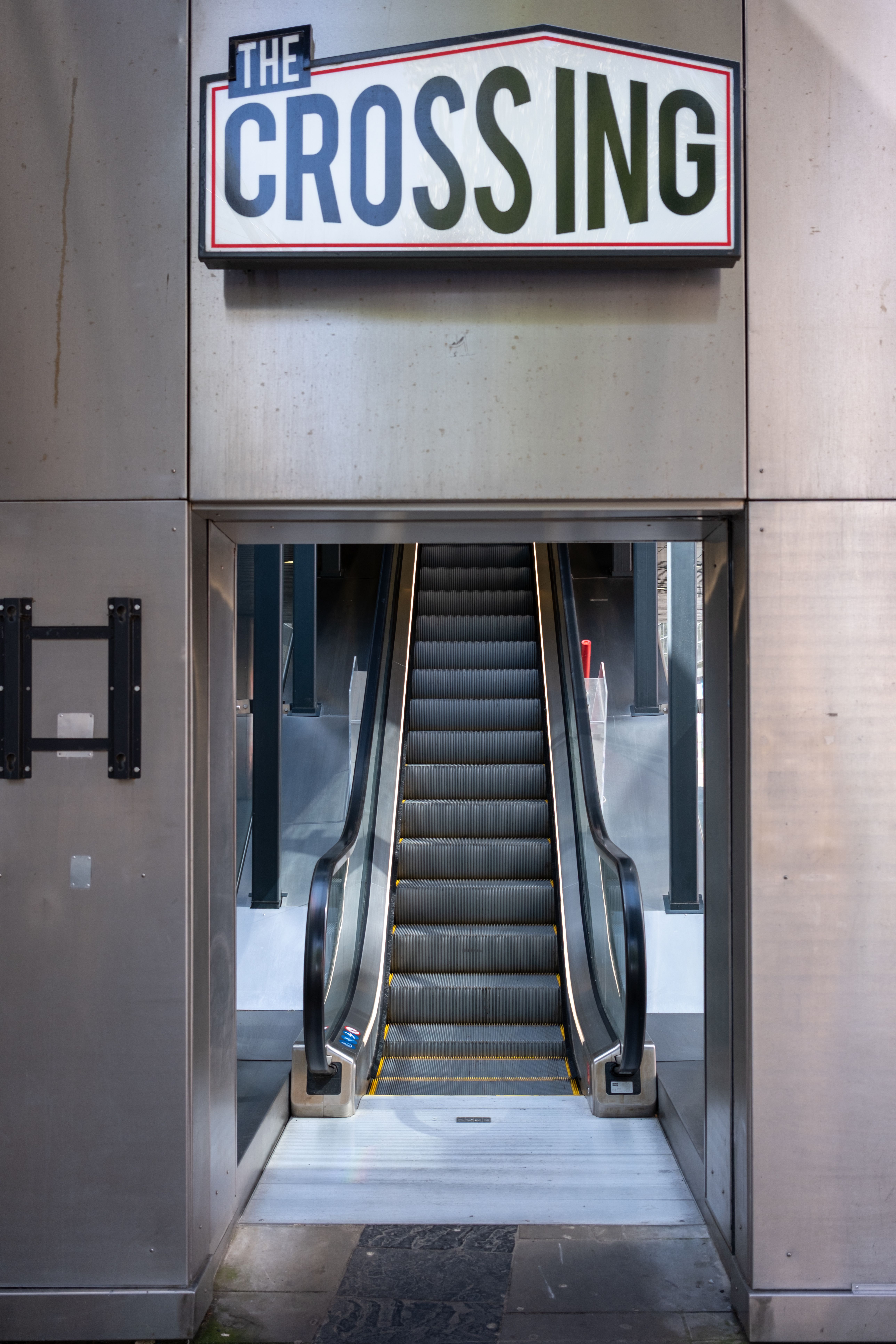 A modern escalator entrance labeled 'The Crossing' in an urban setting, offering a contemporary look.