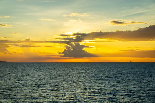 Free Serene ocean sunset view with vibrant yellow sky and dramatic clouds over the water. Stock Photo