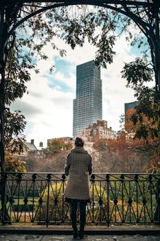 一名女子在公园栏杆旁凝视着秋叶和纽约市的天际线