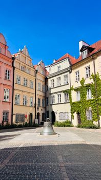 Scenic view of a European courtyard with colorful historic buildings, blue sky, and a bell in the center.