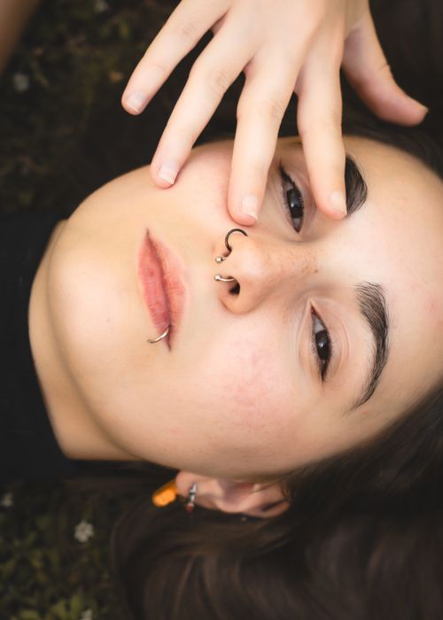 Free Close-up portrait of a young woman with nose and lip piercings, lying on the grass. Stock Photo