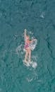 From above of female in bright swimsuit and hat with goggles doing crawl swimming in clear blue water