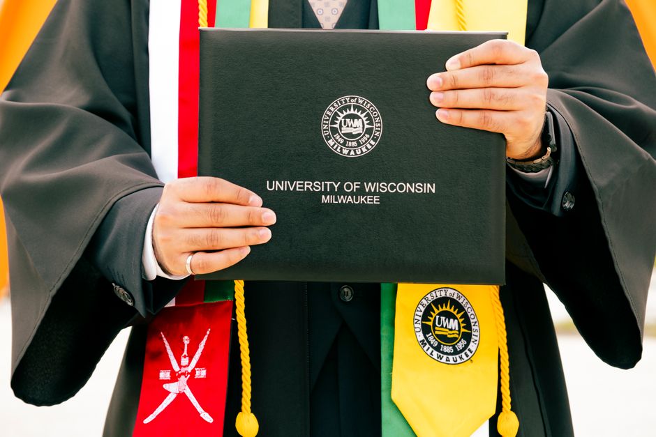 Graduate holding University of Wisconsin-Milwaukee diploma during ceremony.