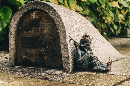Free A whimsical dwarf sculpture leaning against a stone archway in Wrocław, Poland. Stock Photo