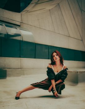 A fashionable woman in a stylish pose outdoors against urban architecture.