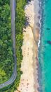 Drone view of peaceful seashore with cars on route in green trees and blue ocean water