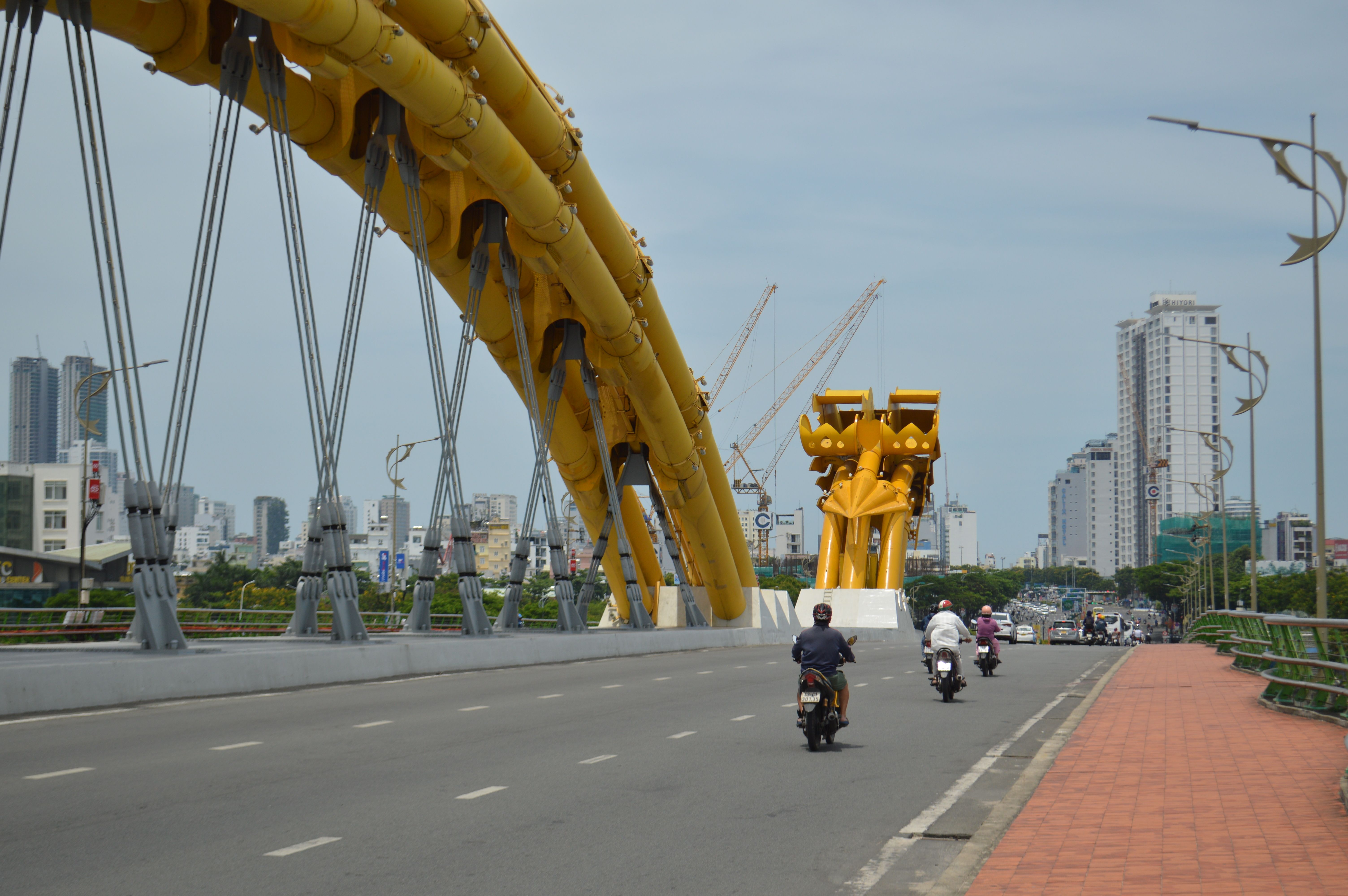 The iconic Dragon Bridge in Da Nang, Vietnam, captured on a sunny day, with motorbikes passing by.