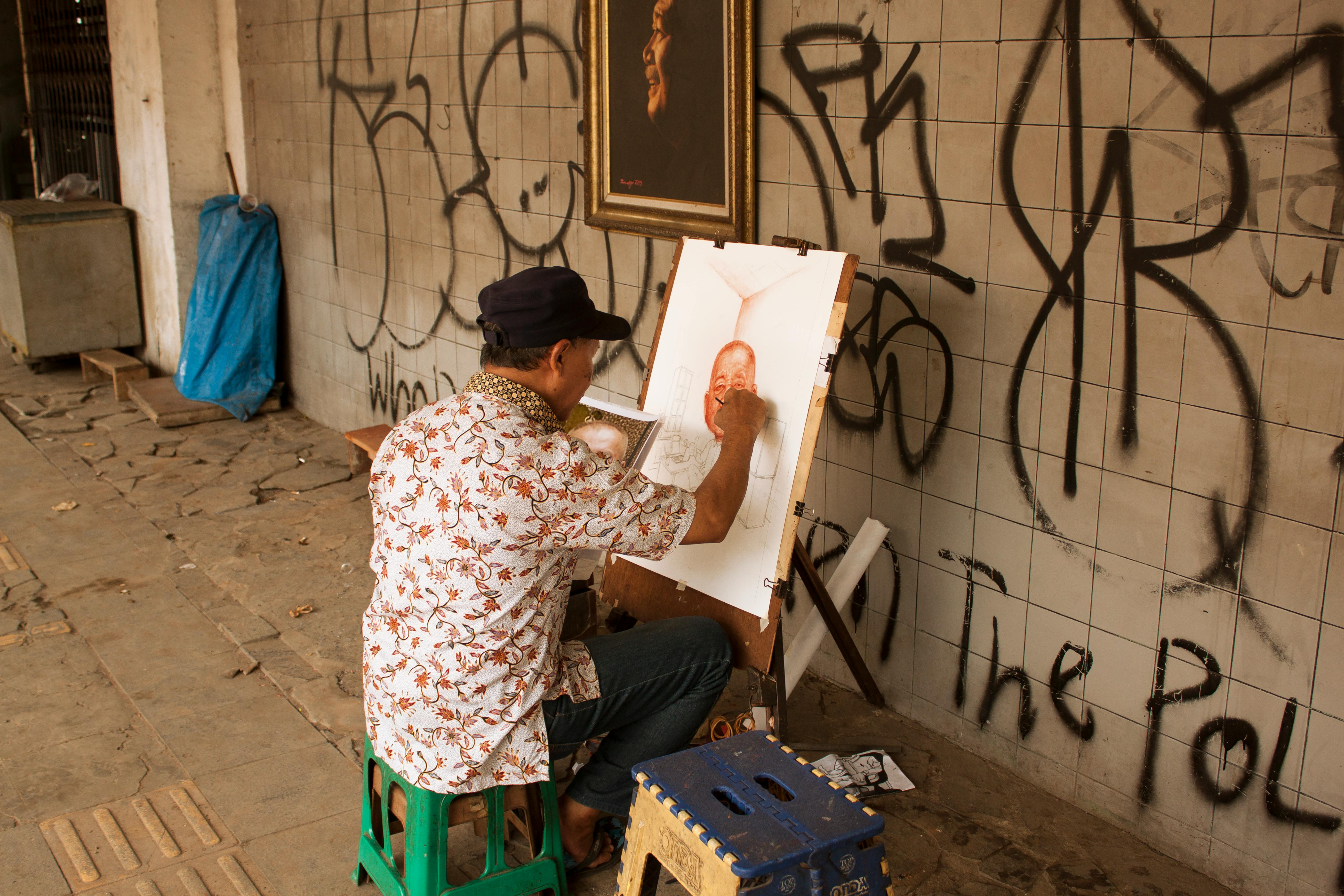 A street artist captures a portrait in an urban area adorned with graffiti.