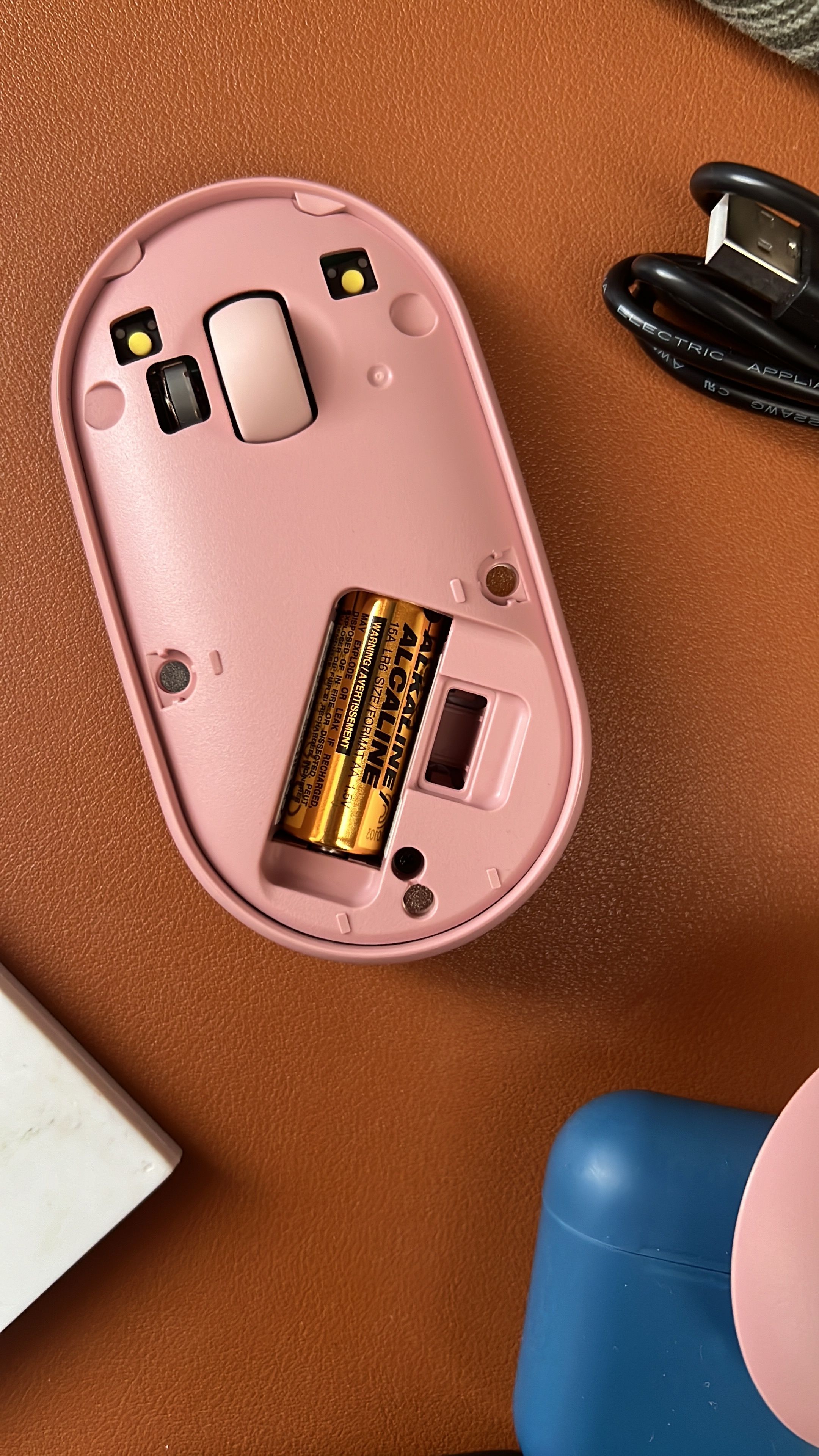 Close-up of an open pink wireless mouse revealing batteries on a desk.