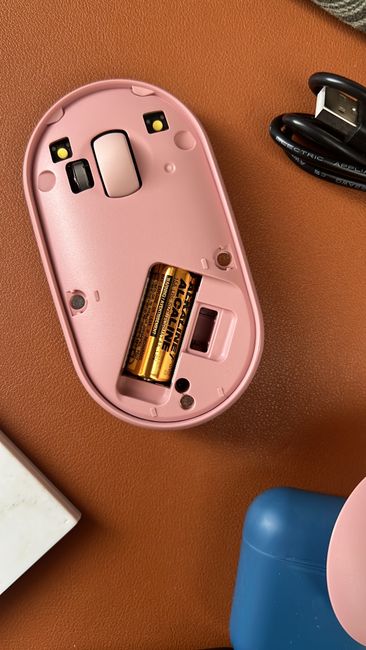 Close-up of an open pink wireless mouse revealing batteries on a desk.