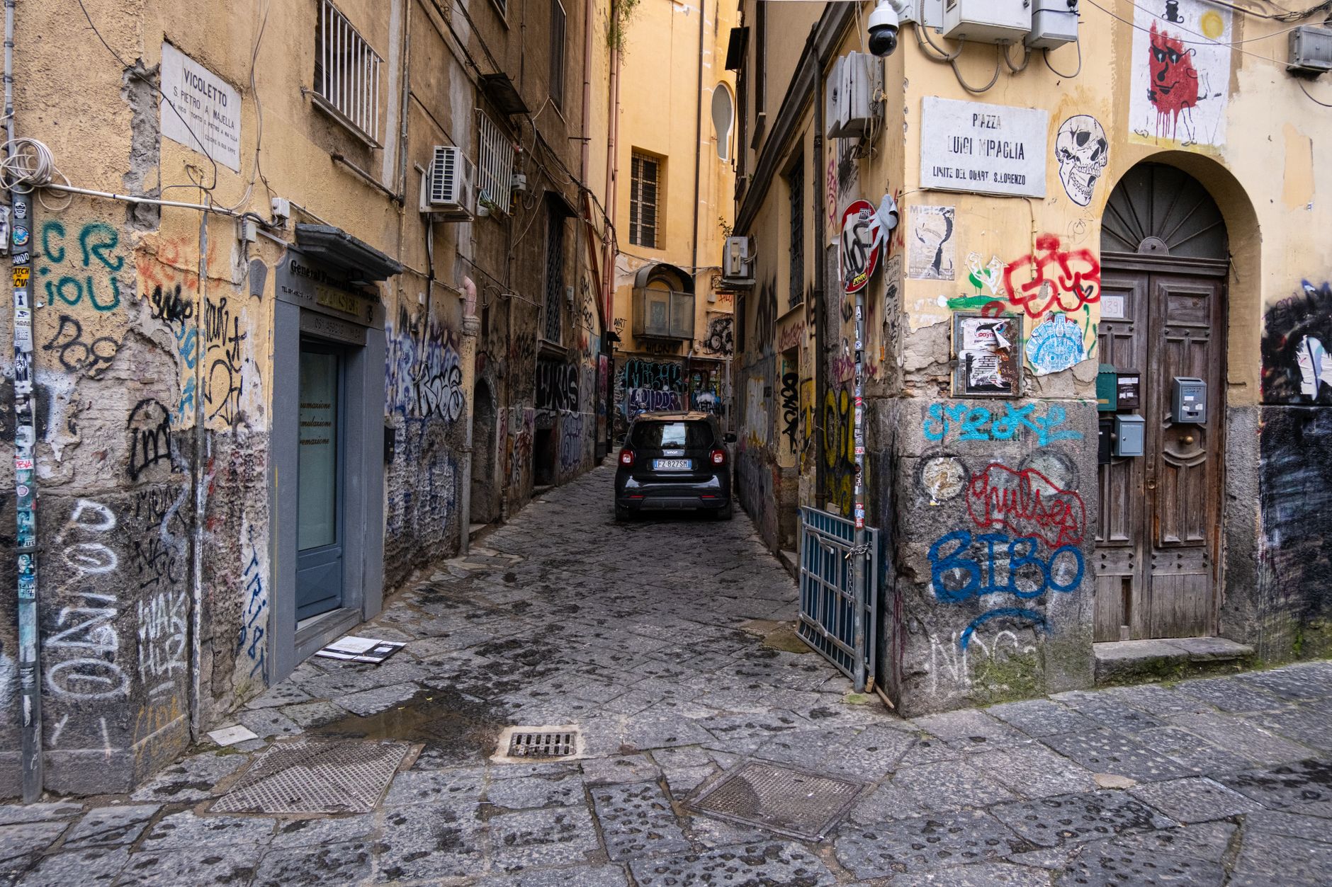 A narrow alley in Naples with colorful graffiti and an old building facade.