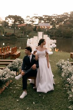 Bride and groom pose elegantly at an outdoor wedding ceremony near a serene lake at sunset.