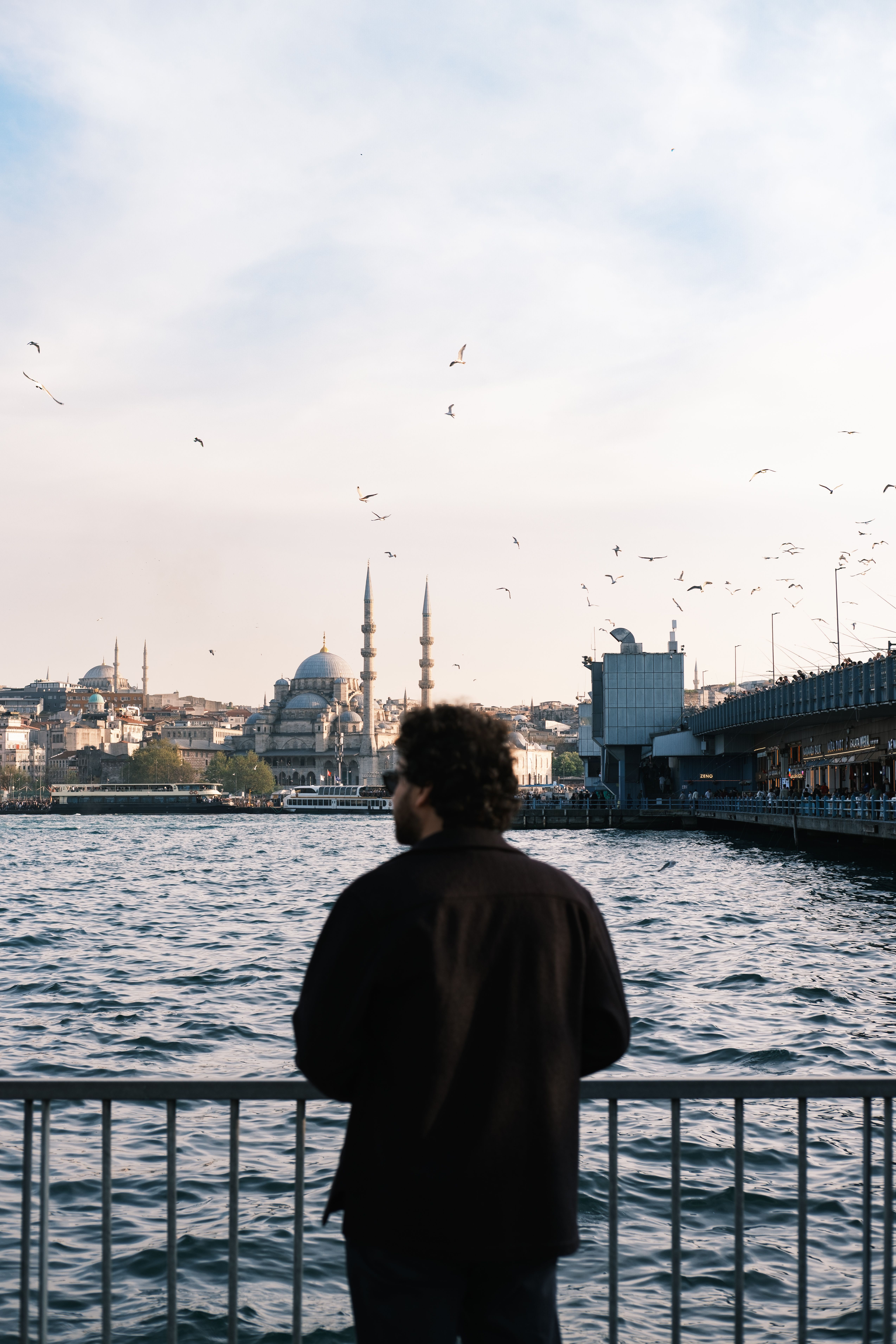 A man gazes across the Bosphorus River, viewing the iconic Istanbul skyline and Yeni Mosque.