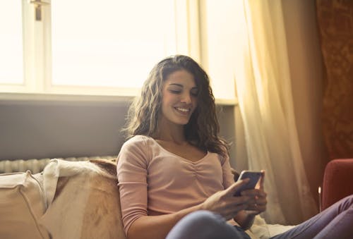 Free Woman Reclining on Bed Using a Smartphone Stock Photo