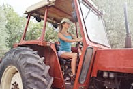 阳光明媚的户外，一名妇女驾驶着红色拖拉机，展示现代农业