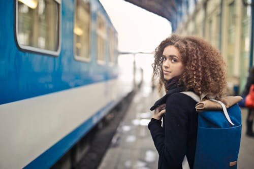 黑色外套站在藍色和白色火車旁邊的女人