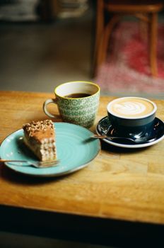 Warm café scene featuring a cappuccino, black coffee, and a slice of nut-topped cake.