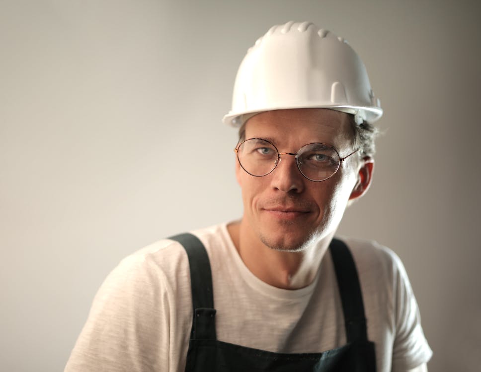 Free Content male builder in workwear and hardhat smiling on gray background in studio and looking at camera Stock Photo
