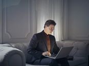在时尚的室内环境中，专业人士坐在沙发上，使用笔记本电脑进行远程工作