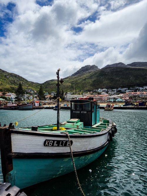 Free A vibrant fishing boat docked in Hout Bay, Cape Town with scenic mountains in the background. Stock Photo