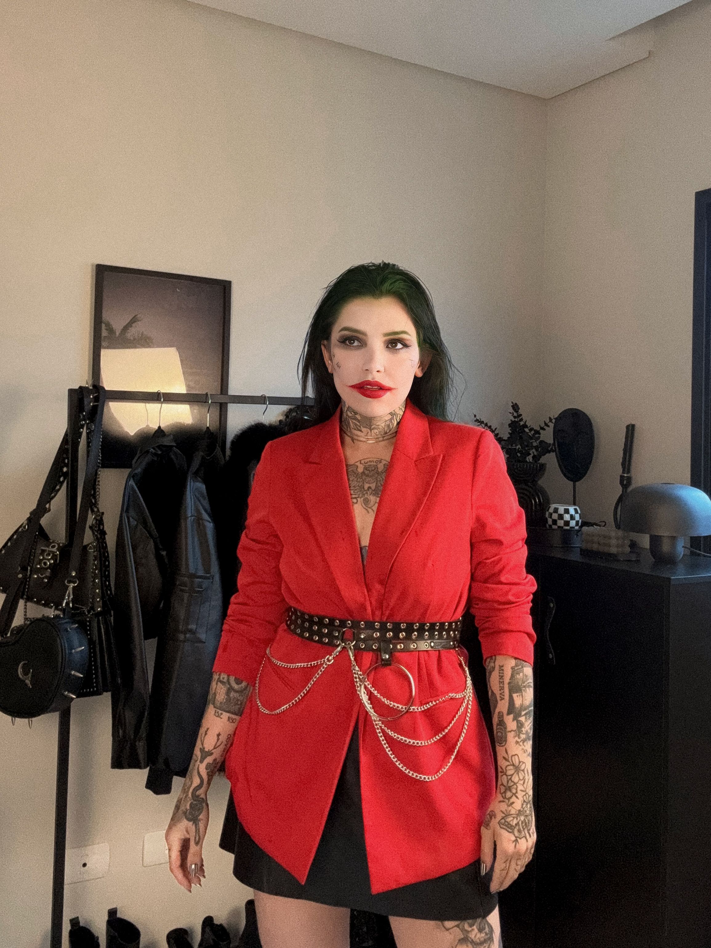 Uma mulher em um ousado traje vermelho com tatuagens e maquiagem, de pé confiantemente dentro de casa.