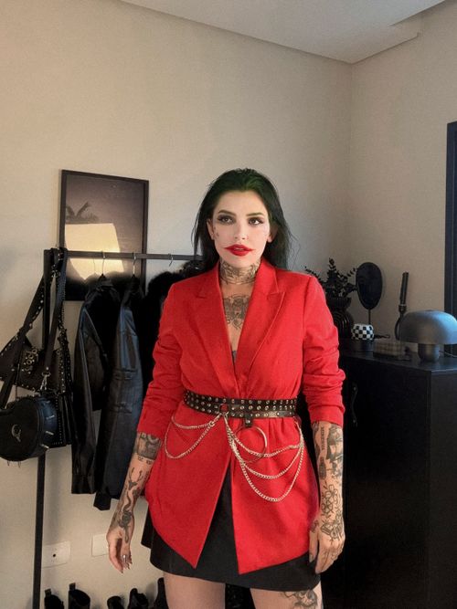 Free A woman in a bold red outfit with tattoos and makeup standing confidently indoors. Stock Photo