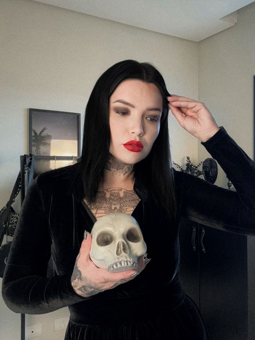 Free Dark gothic portrait of a woman with tattoos holding a skull indoors. Stock Photo