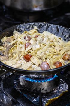 Delicious creamy fettuccine with mushrooms and tomatoes simmering on a stovetop.