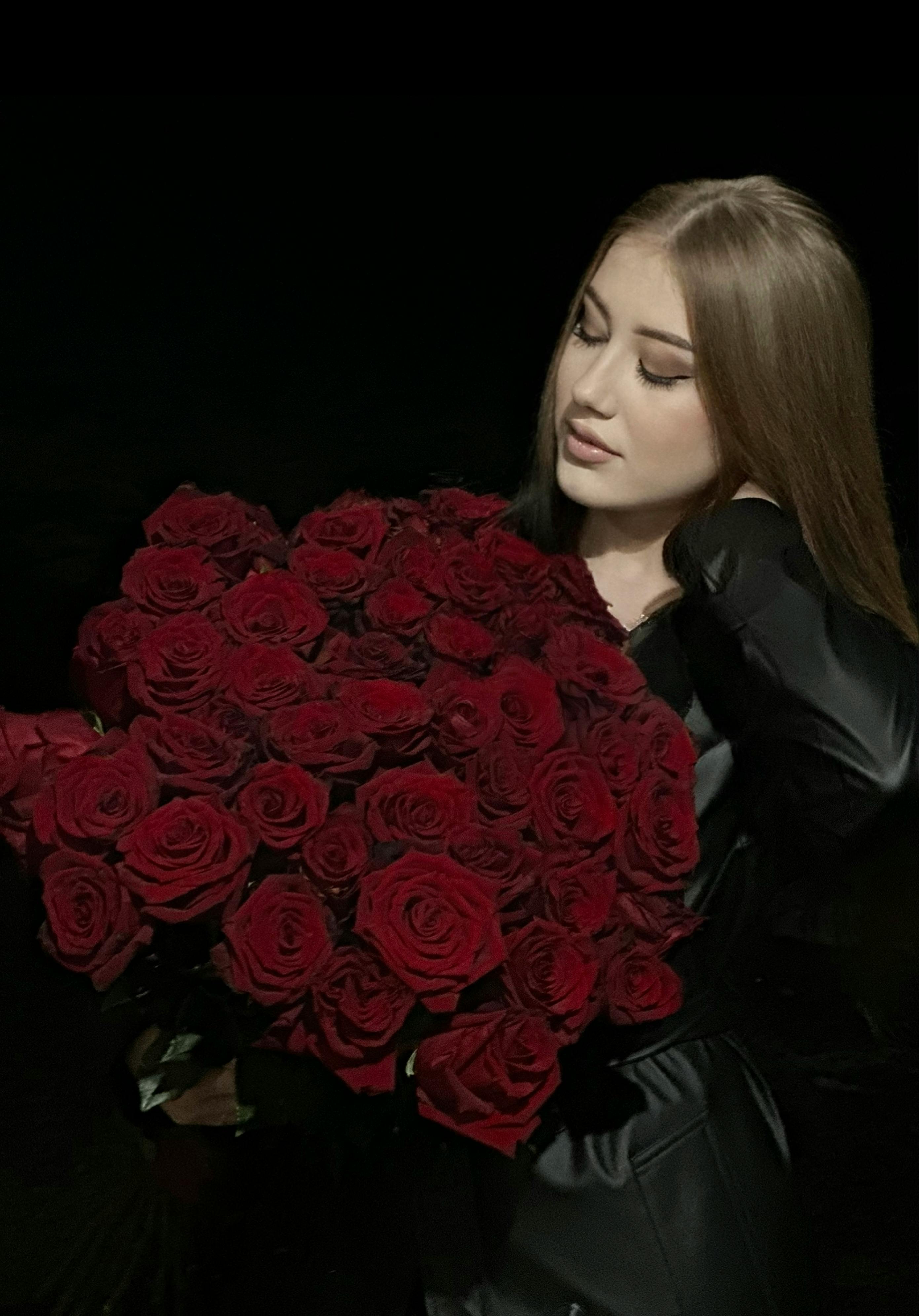 Woman in black attire gracefully holding a bouquet of red roses against a dark background.