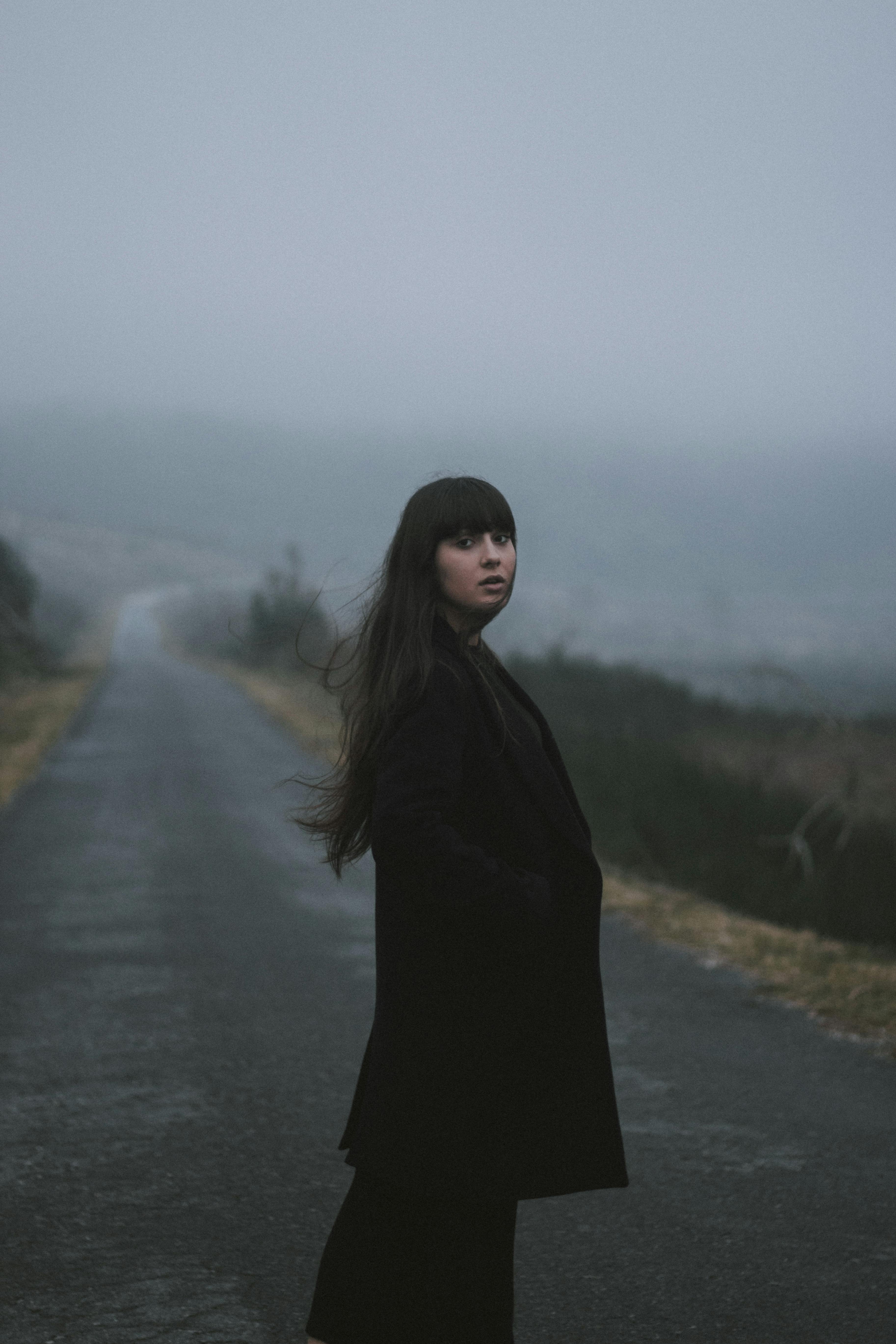 一个女人穿着外套，站在雾蒙蒙的道路上，营造出一种神秘的气氛