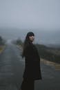 一个女人穿着外套，站在雾蒙蒙的道路上，营造出一种神秘的气氛