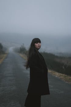 一个女人穿着外套，站在雾蒙蒙的道路上，营造出一种神秘的气氛