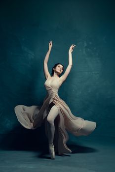 Graceful ballerina performing a dance pose in a flowing dress on a blue backdrop.