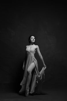 Graceful ballerina in pose, draped gown, studio setting black and white portrait.
