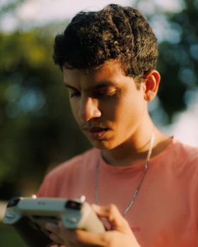Portrait of a young adult male engrossed in mobile gaming outdoors during sunset.
