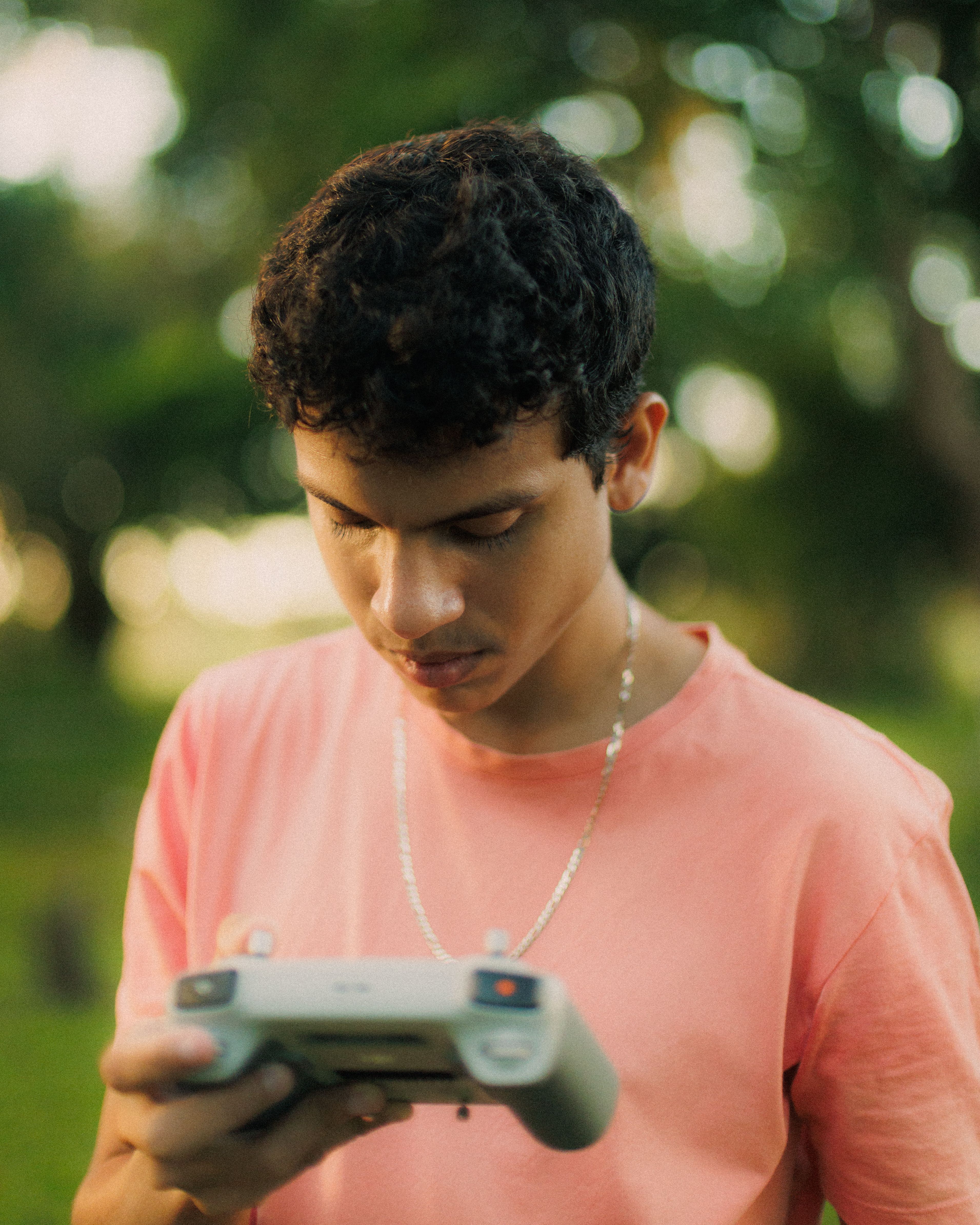A young man examines a drone controller in a sunny, lush environment.