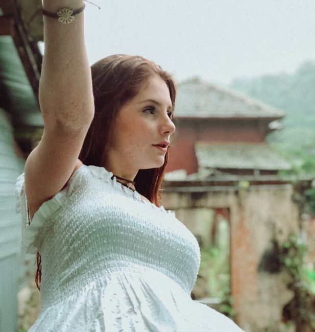 Young woman with long hair enjoys an outdoor view, arm raised, showing a serene expression.