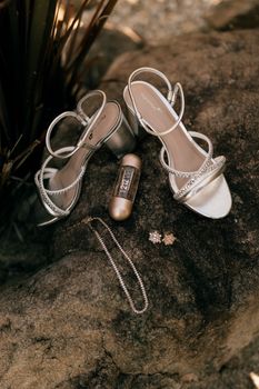 Silver bridal sandals and jewelry elegantly displayed on a rock outdoors.