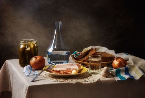 Free A classic still life featuring bread, pickles, and a carafe on a rustic table setting. Stock Photo