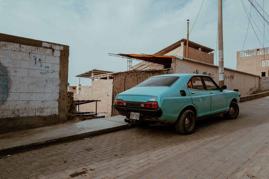 A classic car parked on a cobblestone street in Pacasmayo, Peru, showcasing local architecture.