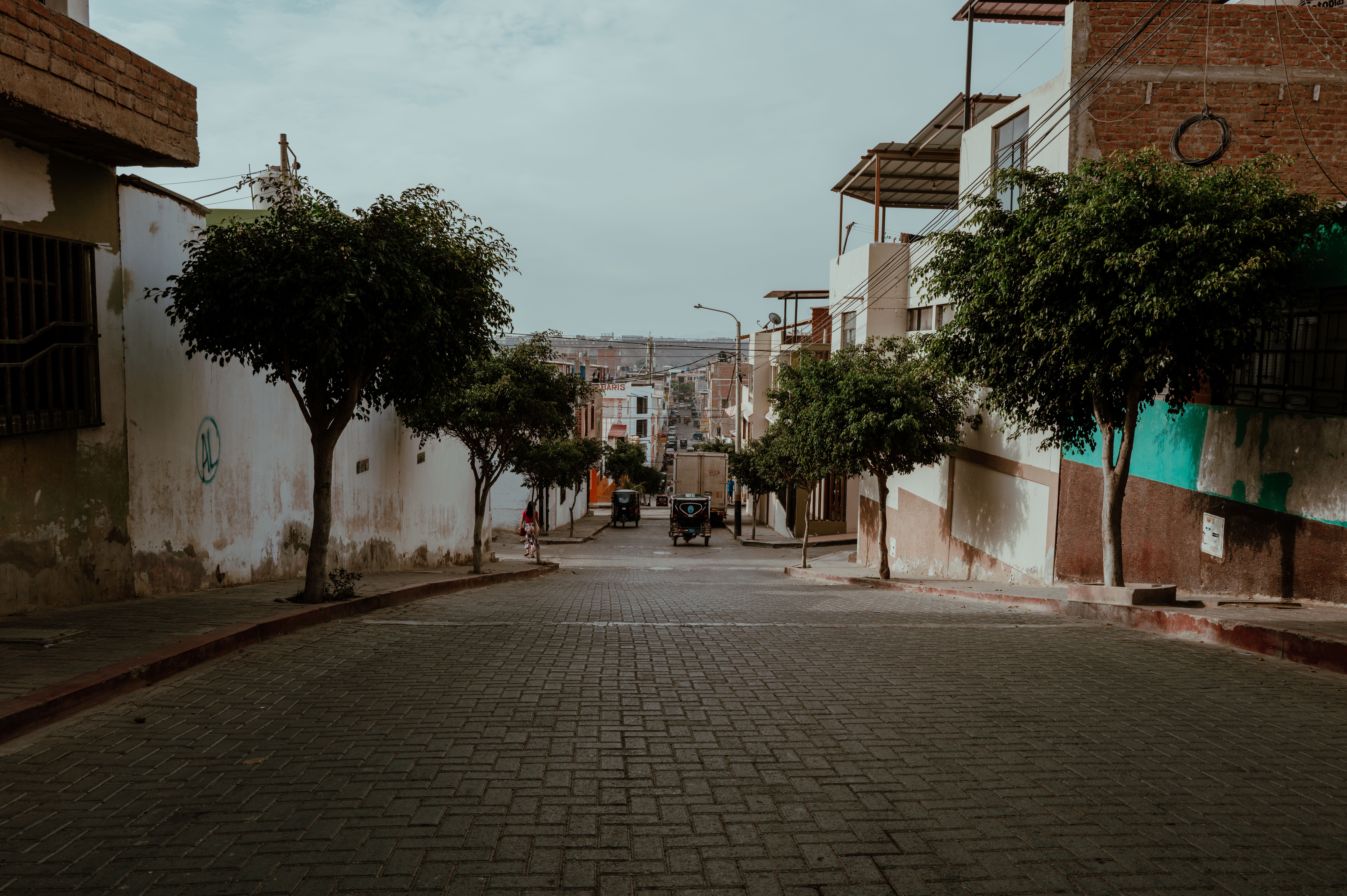 A quiet street in Pacasmayo, Peru, showcasing traditional architecture and urban scenery with trees lining the path.