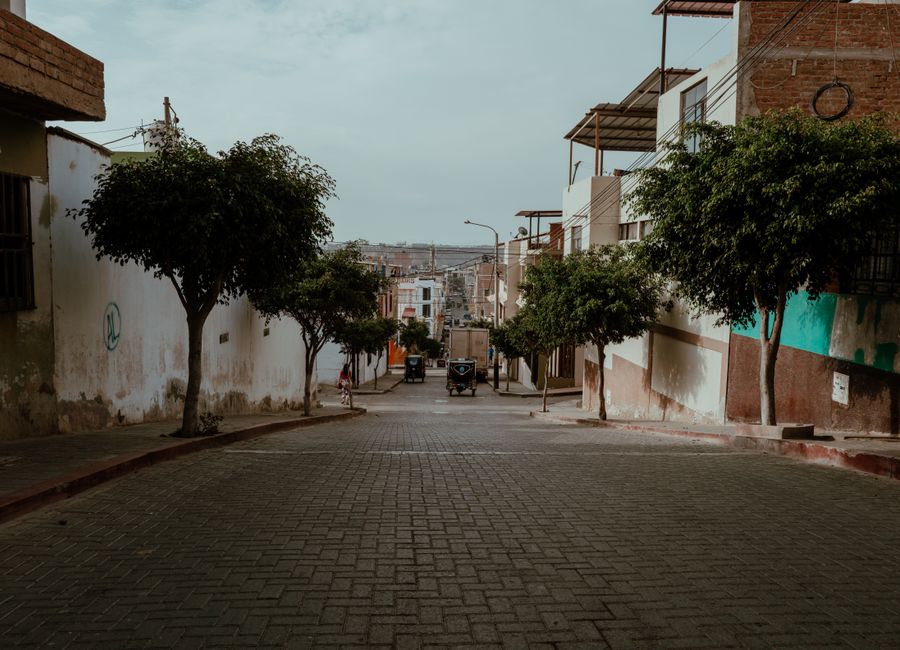 A quiet street in Pacasmayo, Peru, showcasing traditional architecture and urban scenery with trees lining the path.