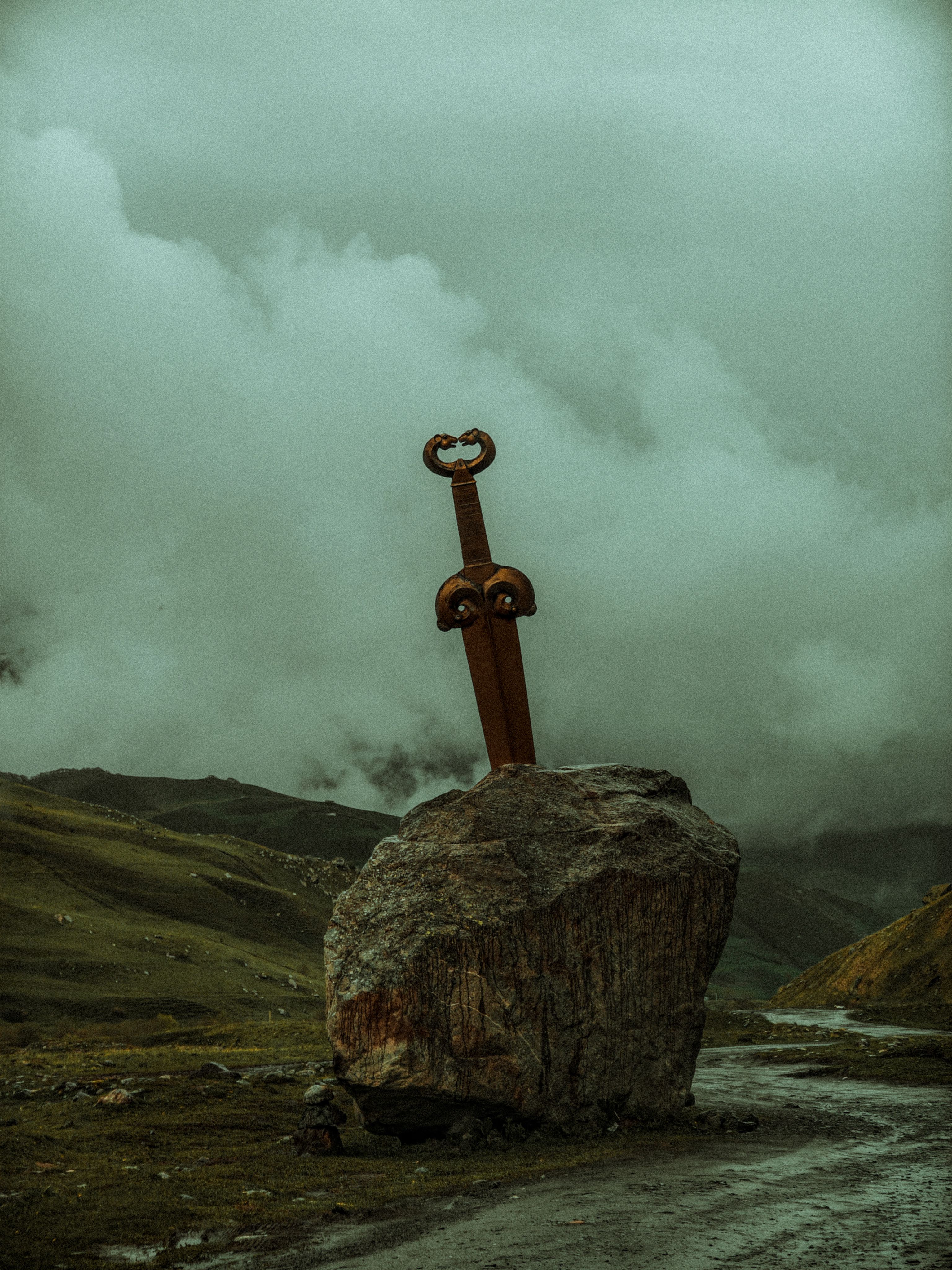 Dramatic image of a large sword monument embedded in a rock on a misty mountain background.