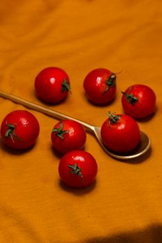 Vibrant cherry tomatoes with a gold spoon on a yellow cloth, showcasing freshness and color.