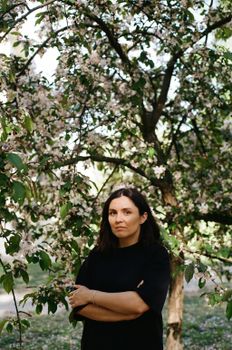 A woman stands among blooming spring trees, creating a serene portrait.
