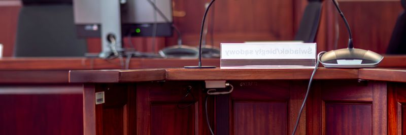 Close-up of a wooden podium with microphones in a Polish courtroom setting.
