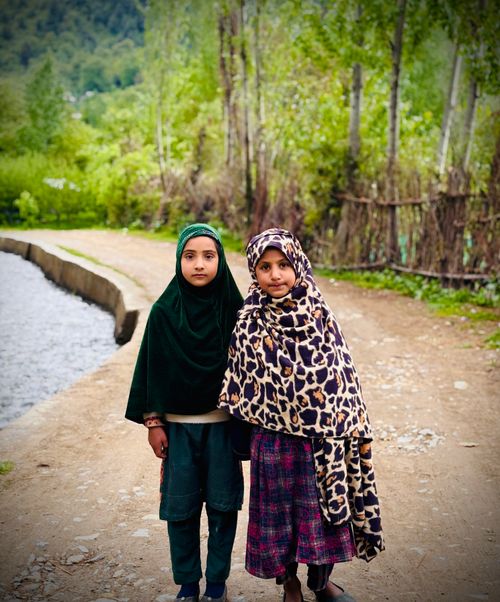 Free Two children in cultural attire stand on a rural path in Kashmir, surrounded by lush greenery. Stock Photo